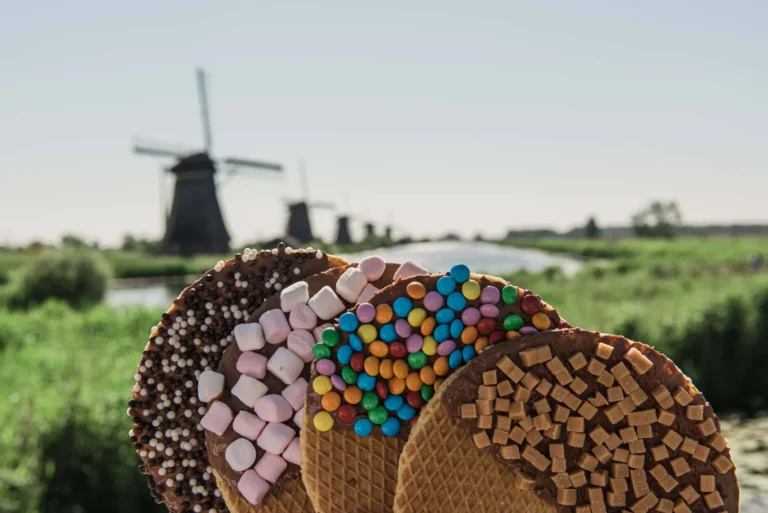 Hand holding stroopwafels with chocolate and colourful toppings in front of the Kinderdijk windmills