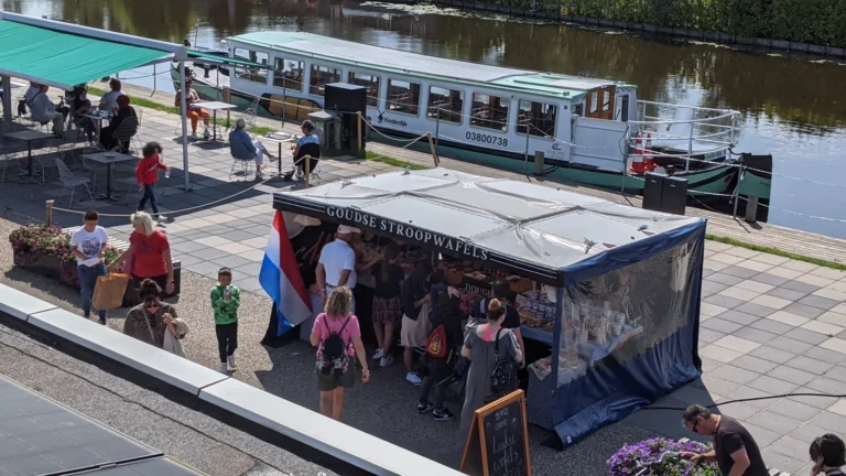 Visitors at the Dough stroopwafel stall by the water in Kinderdijk, with a tour boat behind it